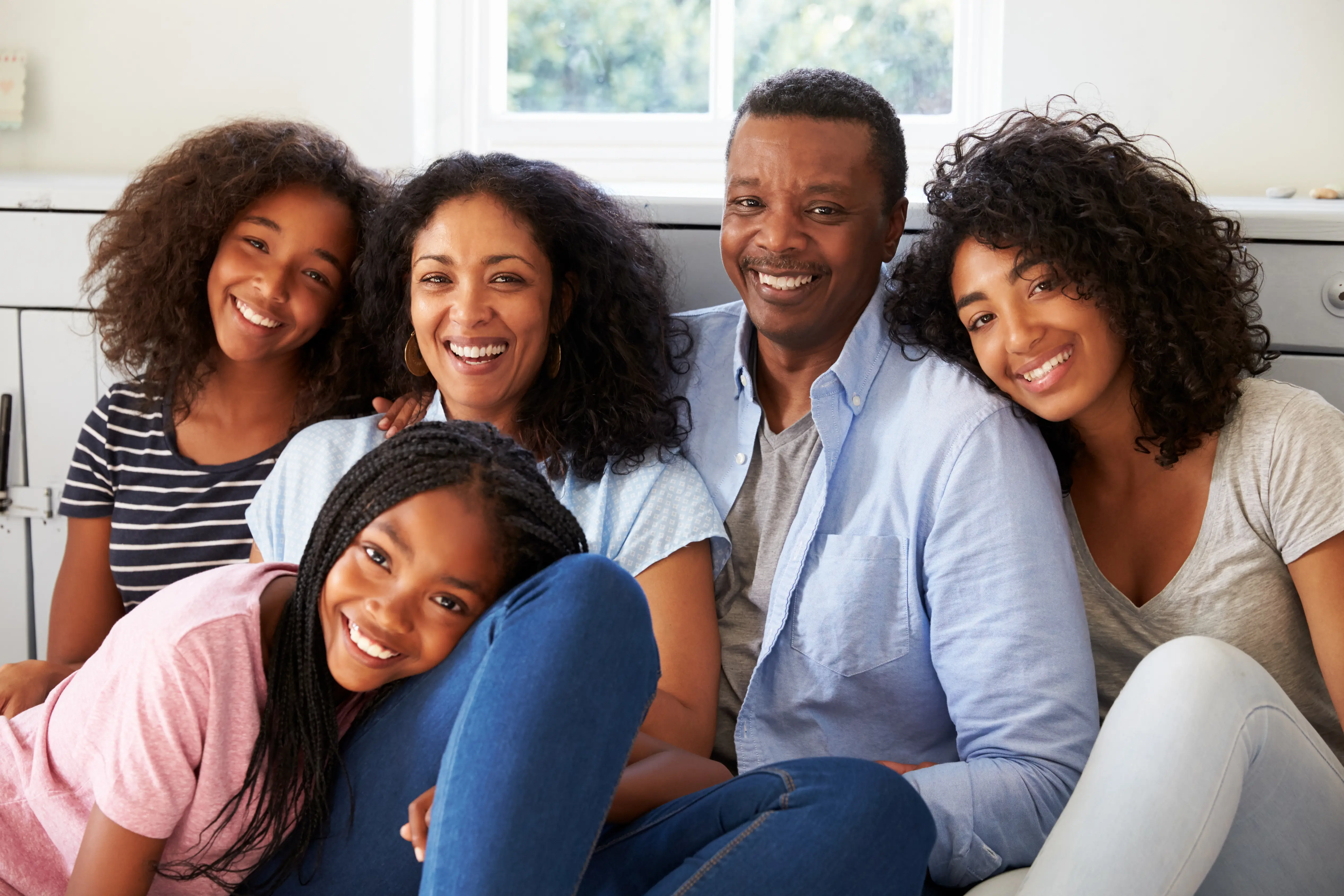 Portrait Of Smiling Ethnic Family Relaxing On Seat At Home