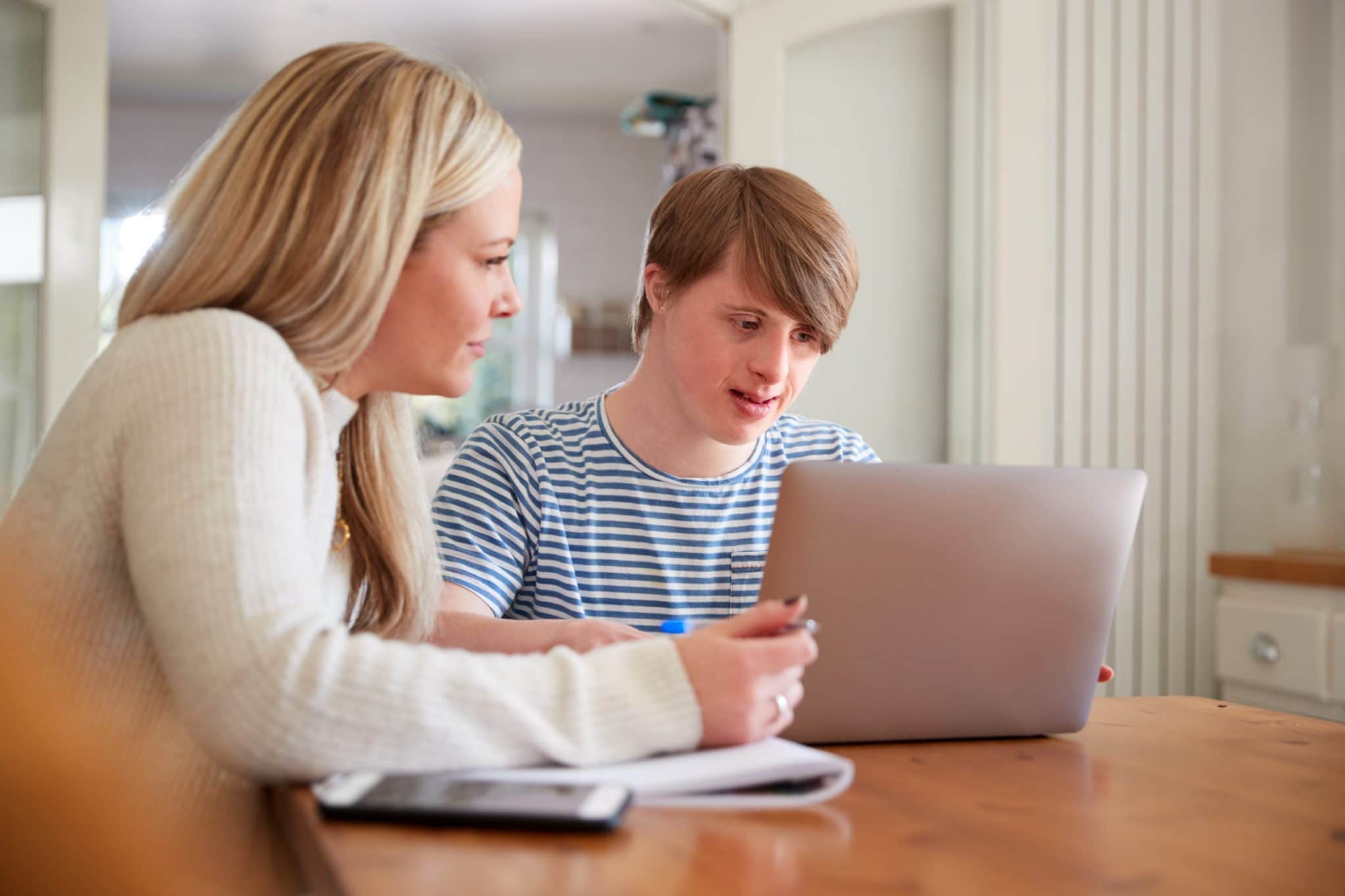 Downs Syndrome Man Sitting With Home Tutor Using Laptop For Lesson At Home